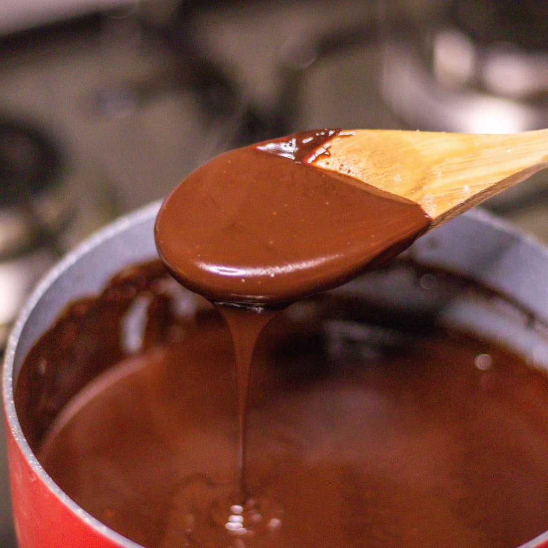 Wooden spoon lifting a spoonful of chocolate sauce from a pot.