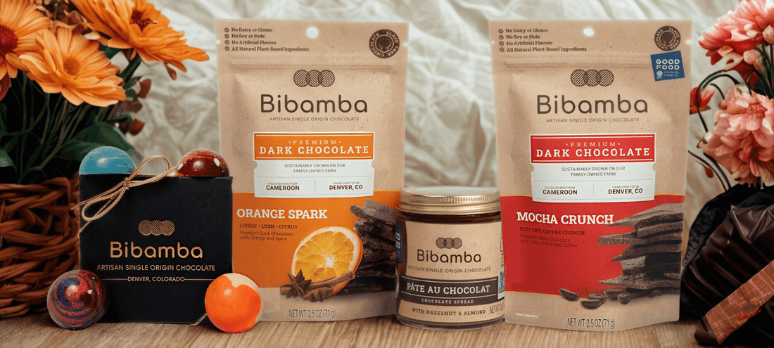 Bibamba chocolate products including bags and a bar on a wooden surface with flowers in the background.