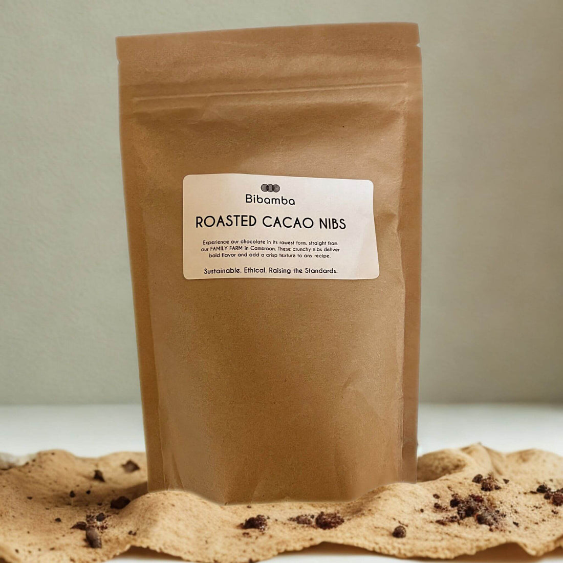 Brown paper bag of Bibamba roasted cacao nibs on a light surface with a neutral background