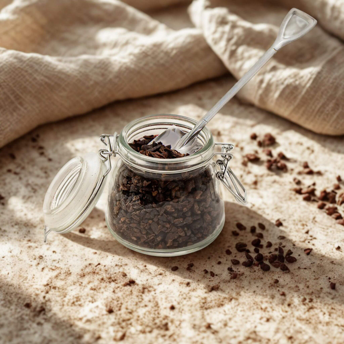 Glass jar with coffee beans and a spoon on a textured surface