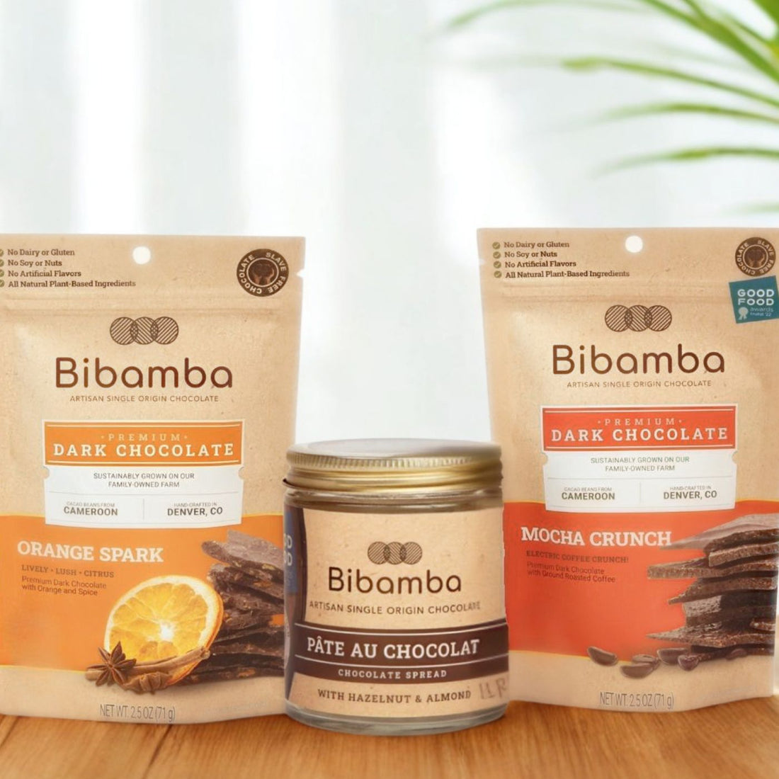 Bibamba chocolate products including packages and a jar of pate on a wooden surface with a white background.