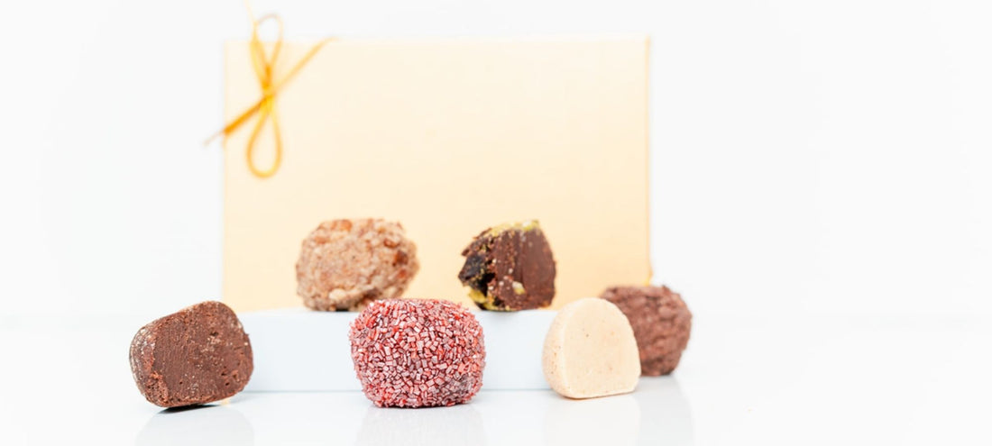 Assorted chocolate truffles on a white surface with a gold box in the background.