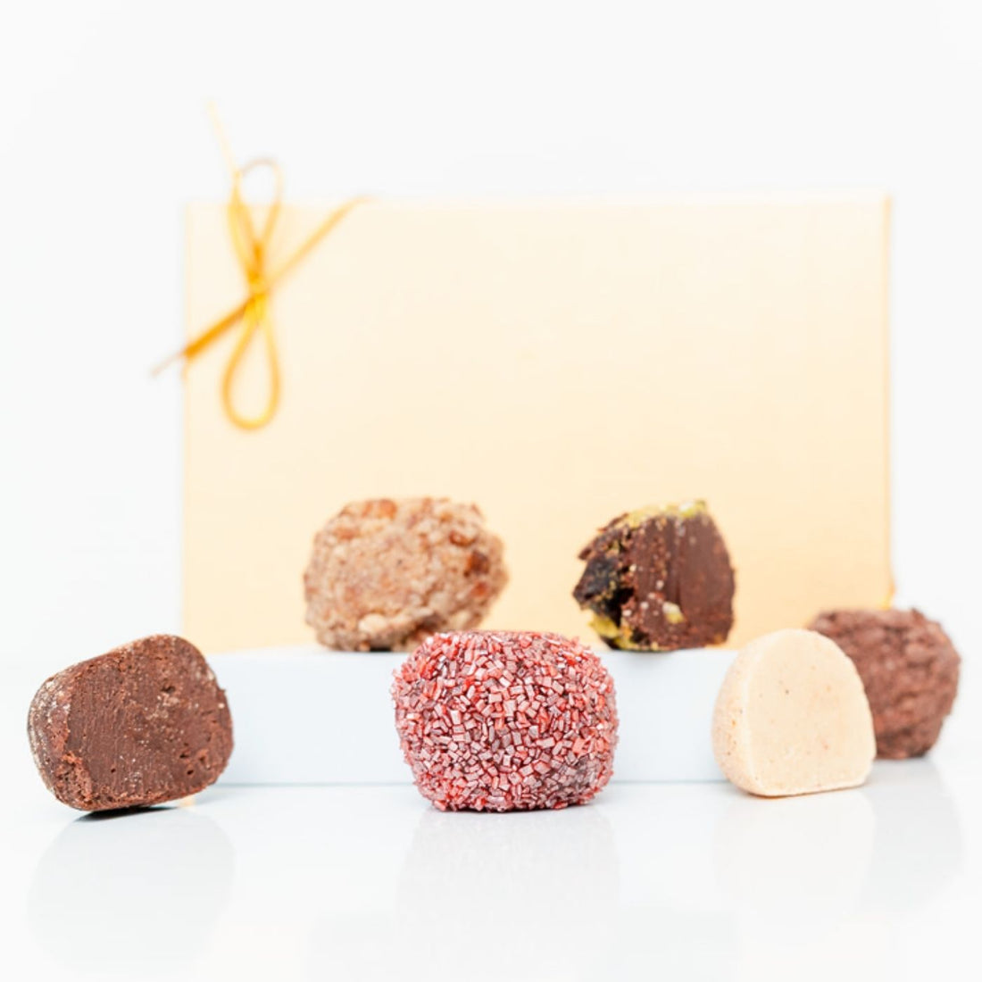 Assorted chocolate truffles in front of a gold box on a white background